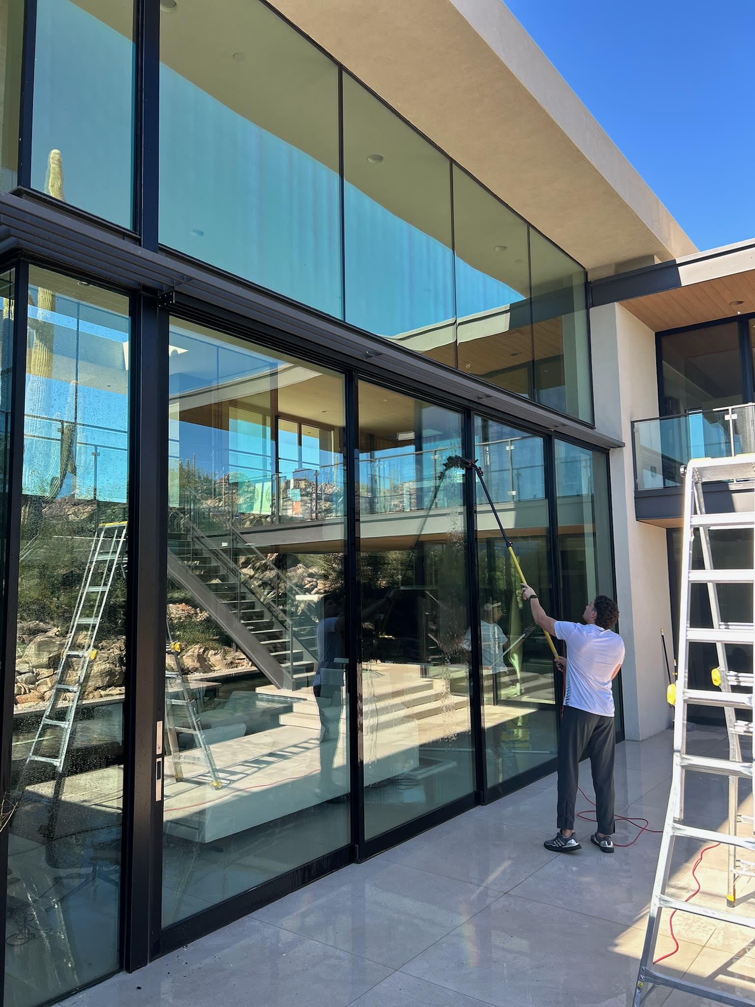 TrueBlue technician cleaning floor-to-ceiling glass on a modern Tucson home with a water-fed pole